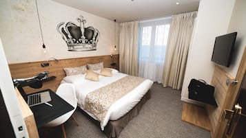 A hotel room with a bed, a desk with a laptop, a TV, and a crown mural on the wall.