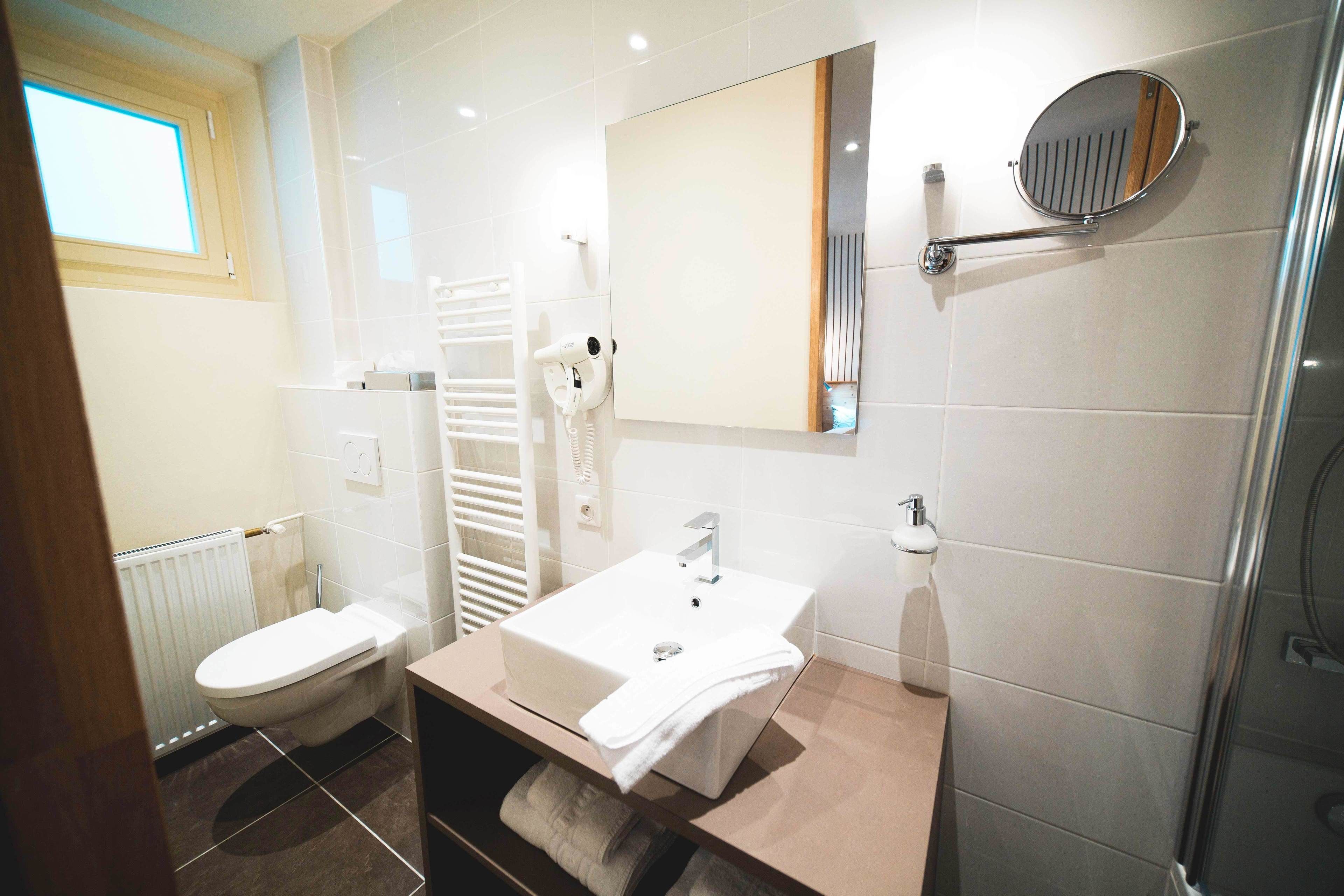 Ein modernes Badezimmer mit einem weißen Waschbecken, einem Spiegel, einem Handtuchhalter und einer Toilette.
