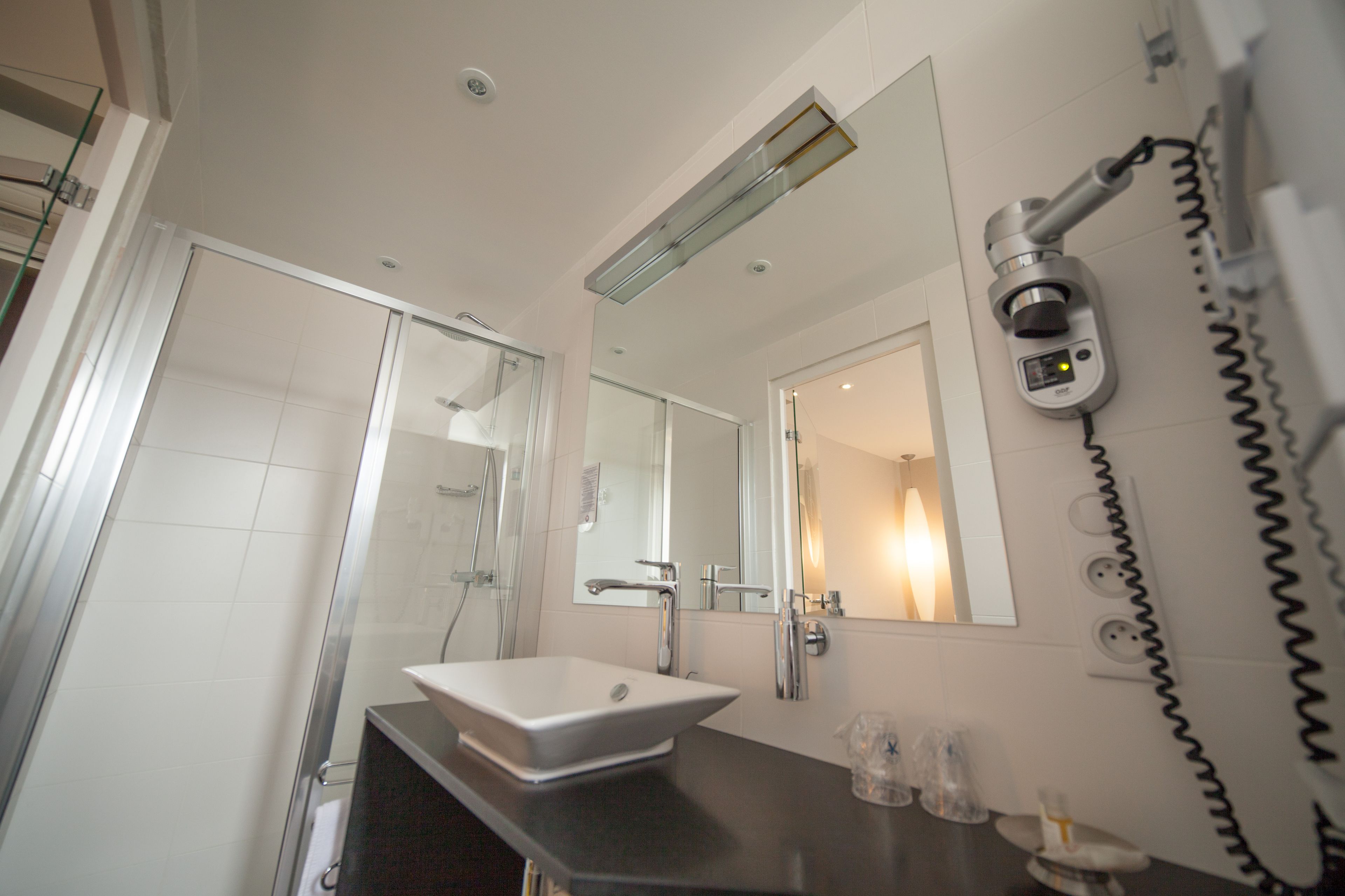 Une salle de bain moderne avec une douche à parois de verre, un lavabo blanc et un sèche-cheveux fixé au mur.
