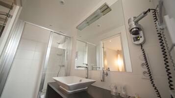 A modern bathroom with a glass shower enclosure, a white sink, and a hairdryer mounted on the wall.