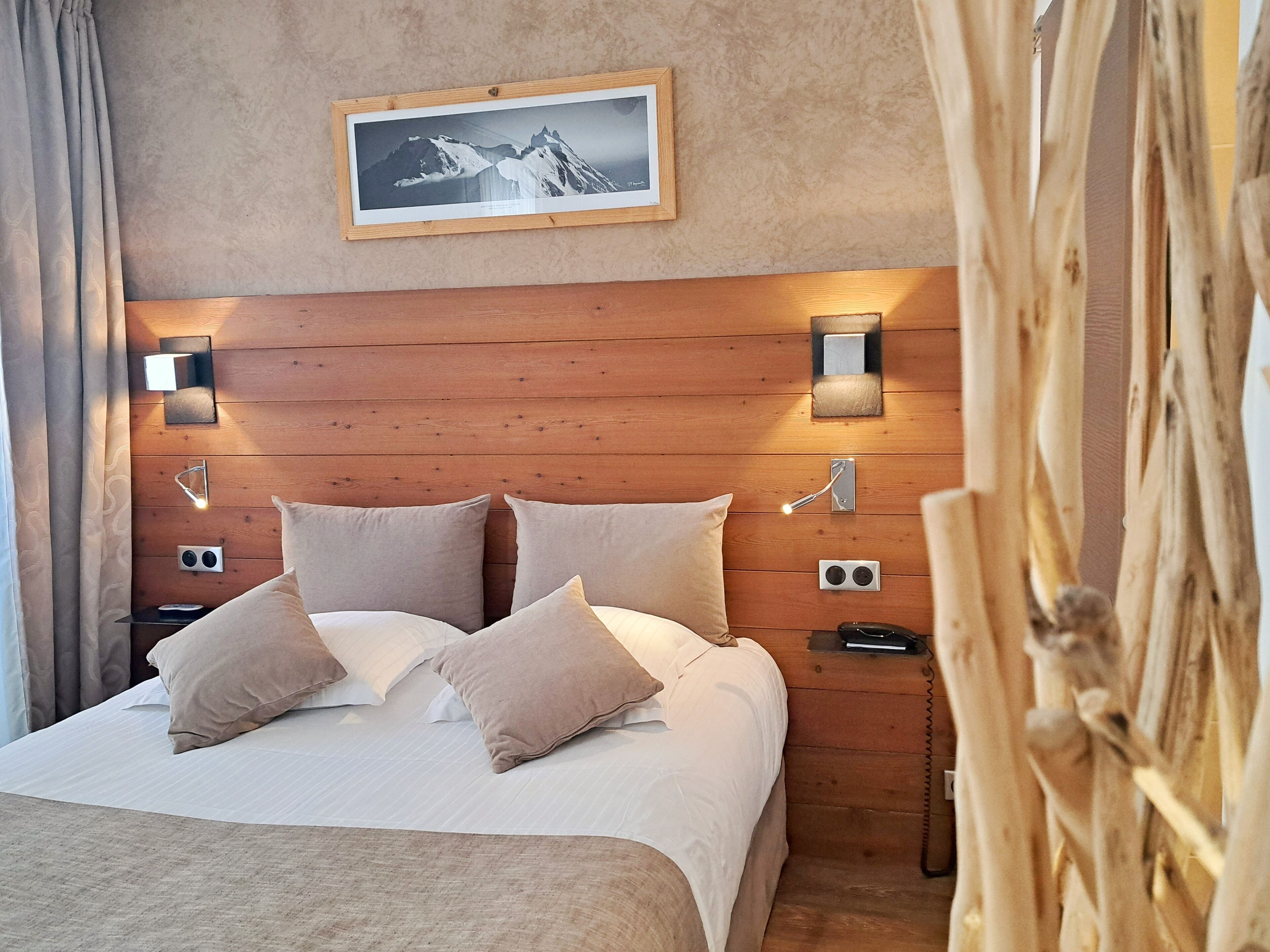 Un dormitorio con cabecera de madera, un cuadro enmarco, lámparas de noche y una cama con almohadas.