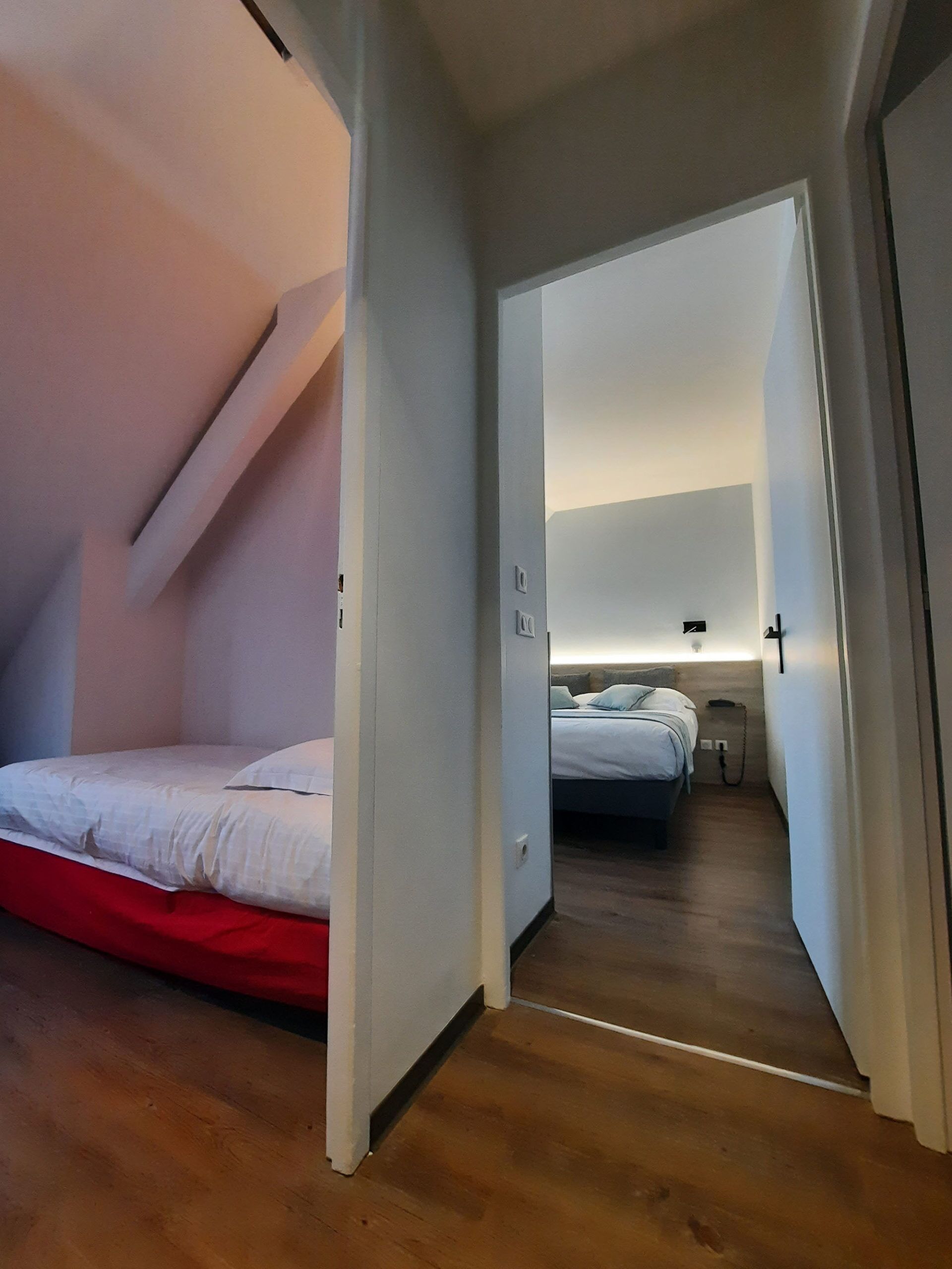 Ein Schlafzimmer mit roter Bettdecke, Holzboden und weißer Decke.