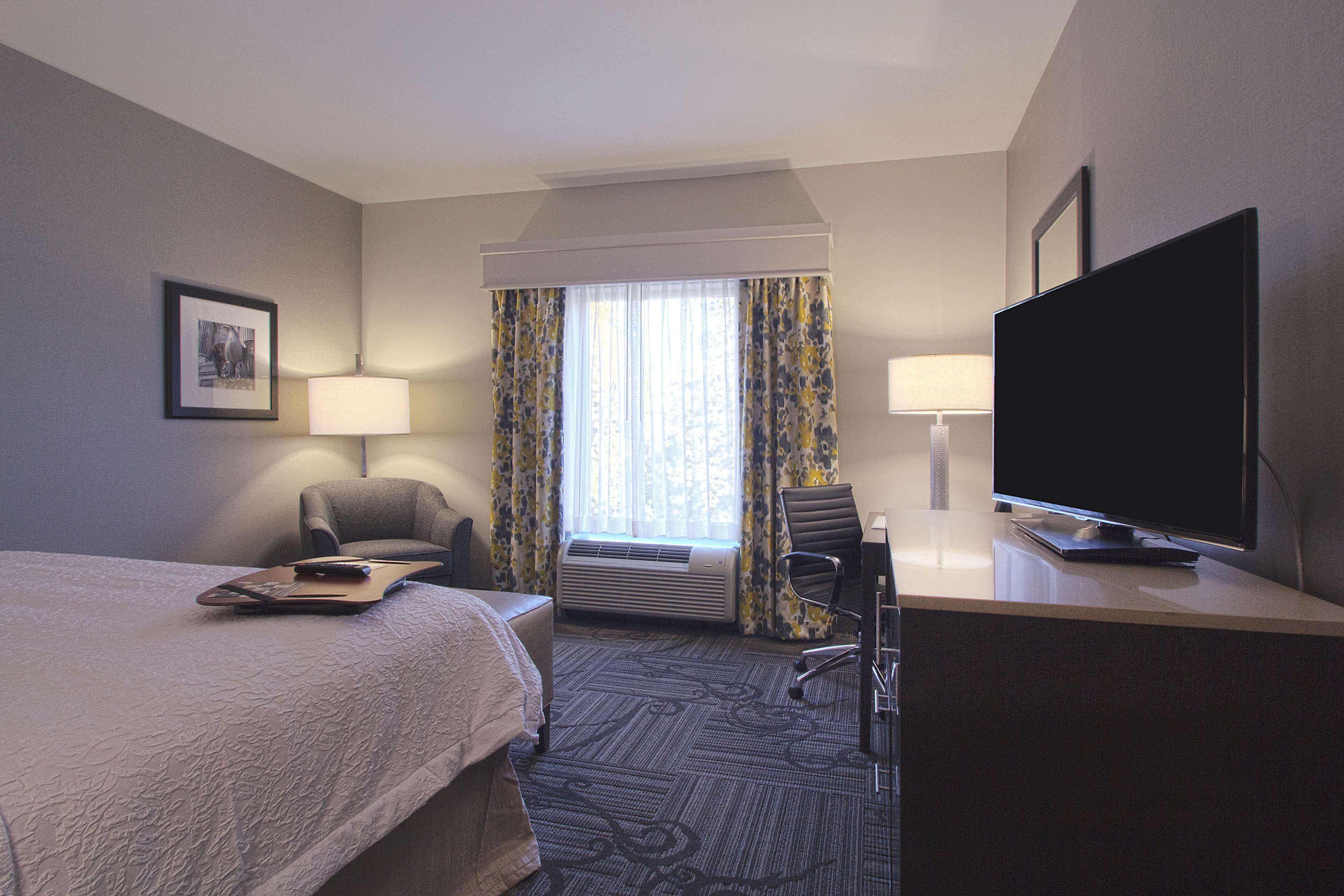 Habitación de hotel con cama, dos sillas, escritorio con televisor y ventana con cortinas.