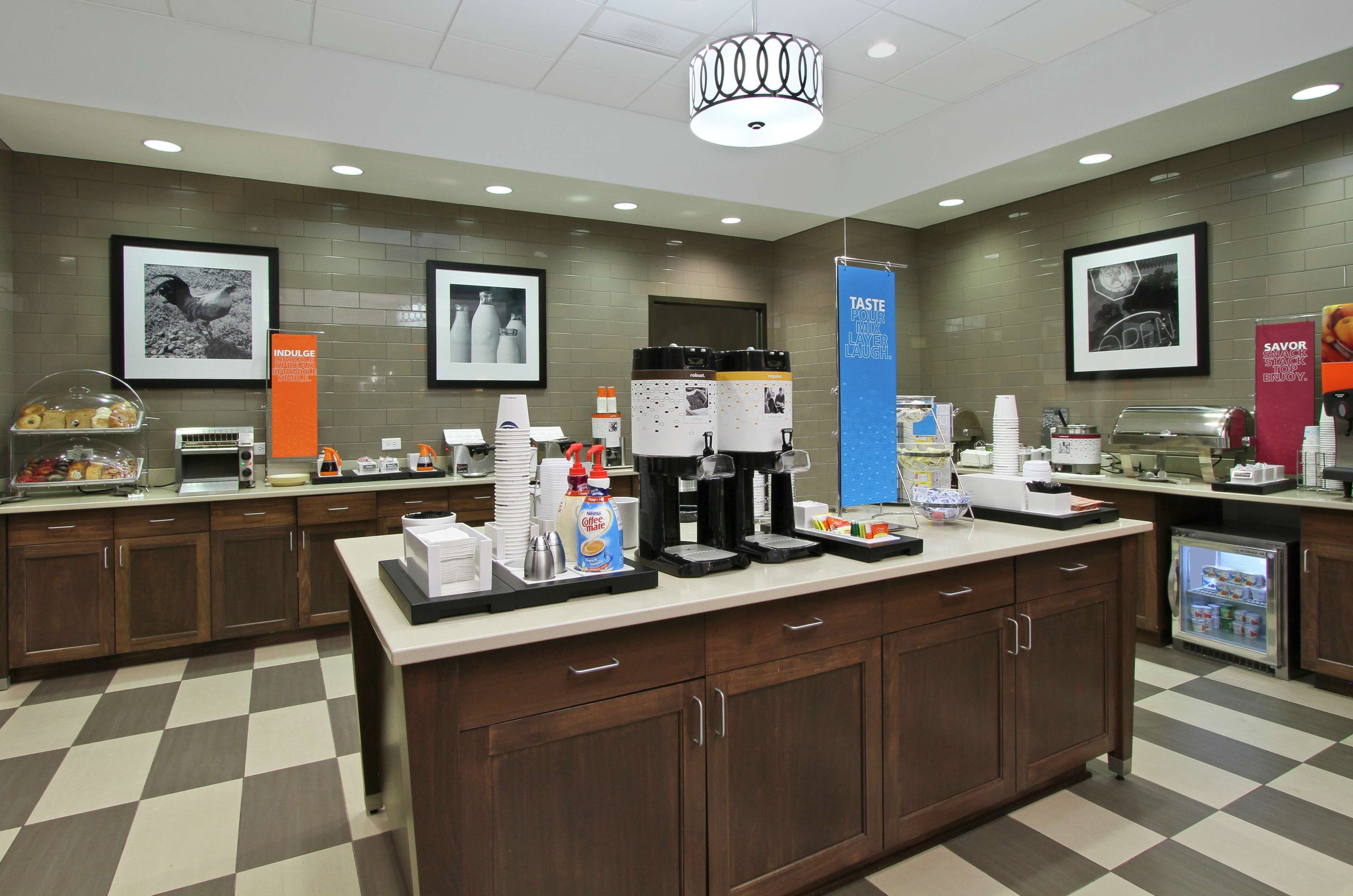 A modern hotel kitchen with a checkered floor, coffee machines, and a refrigerator.