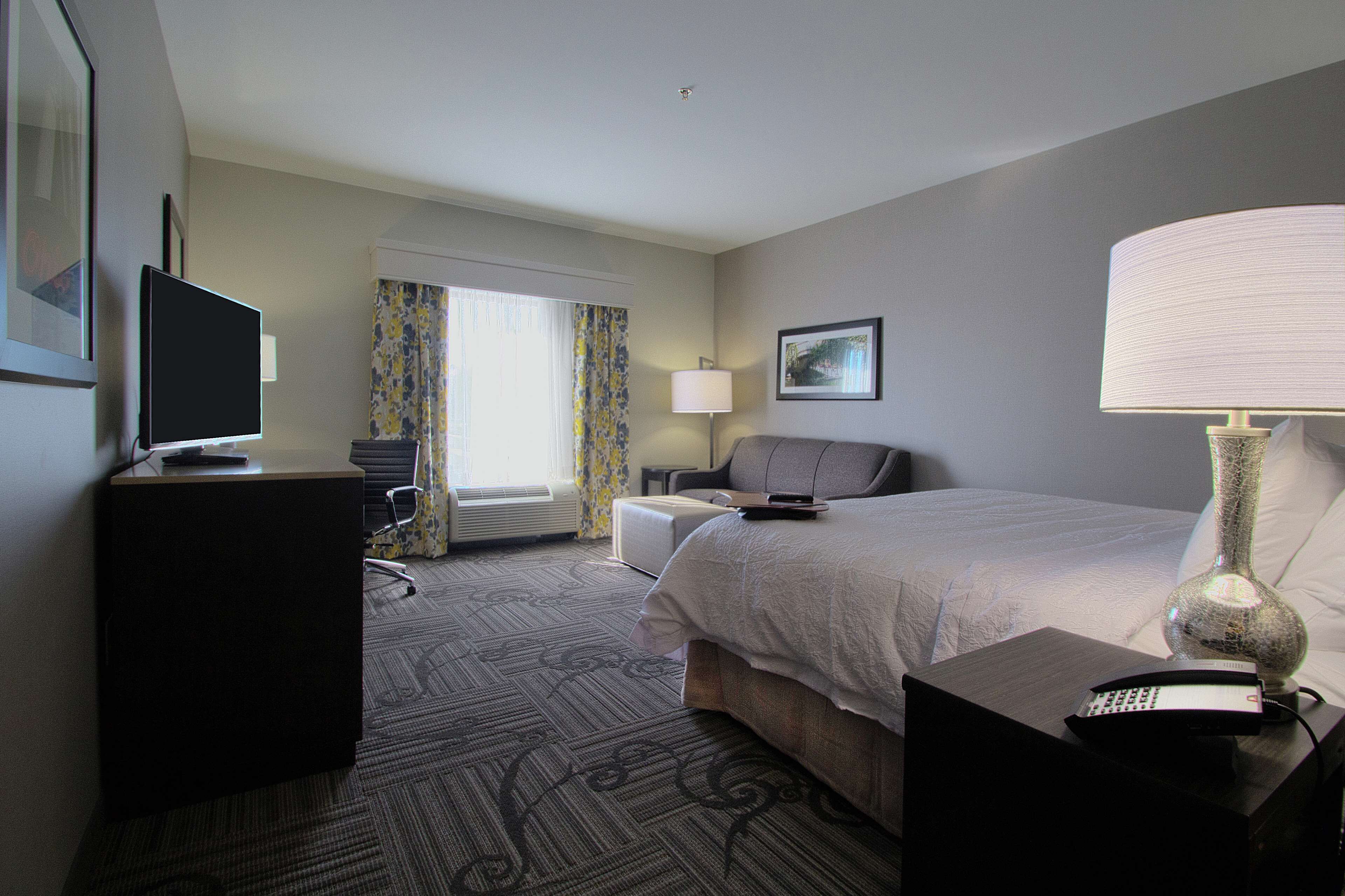 A hotel room with a bed, a desk with a computer, a chair, a lamp, and a television.