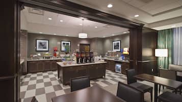 A hotel lobby with a checkered floor, a central island with coffee machines, and seating areas.