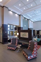 A lobby with two patterned armchairs, a small round table, a fireplace, and a large window.