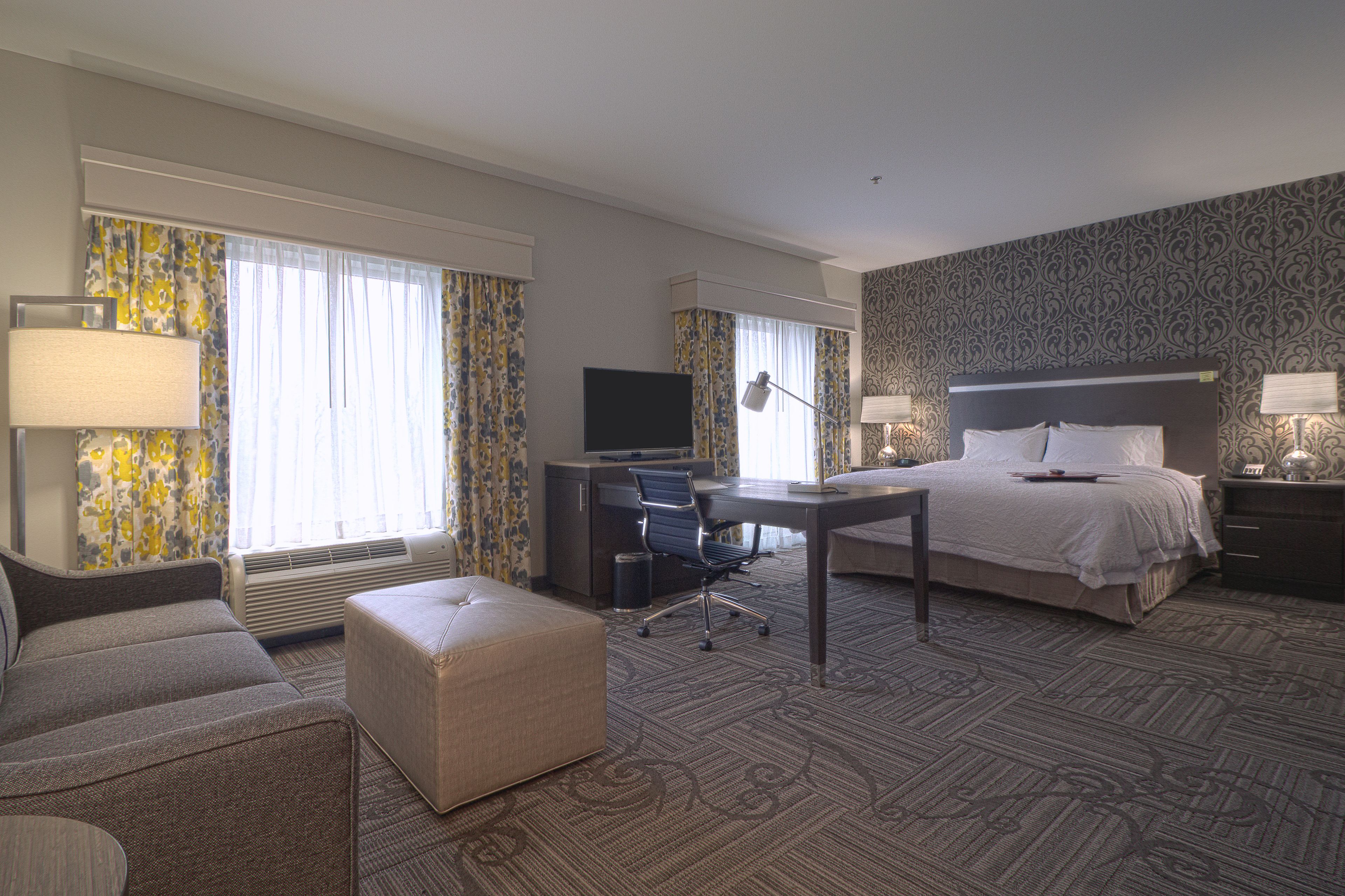 A hotel room with a bed, a desk, a chair, a couch, and a television.