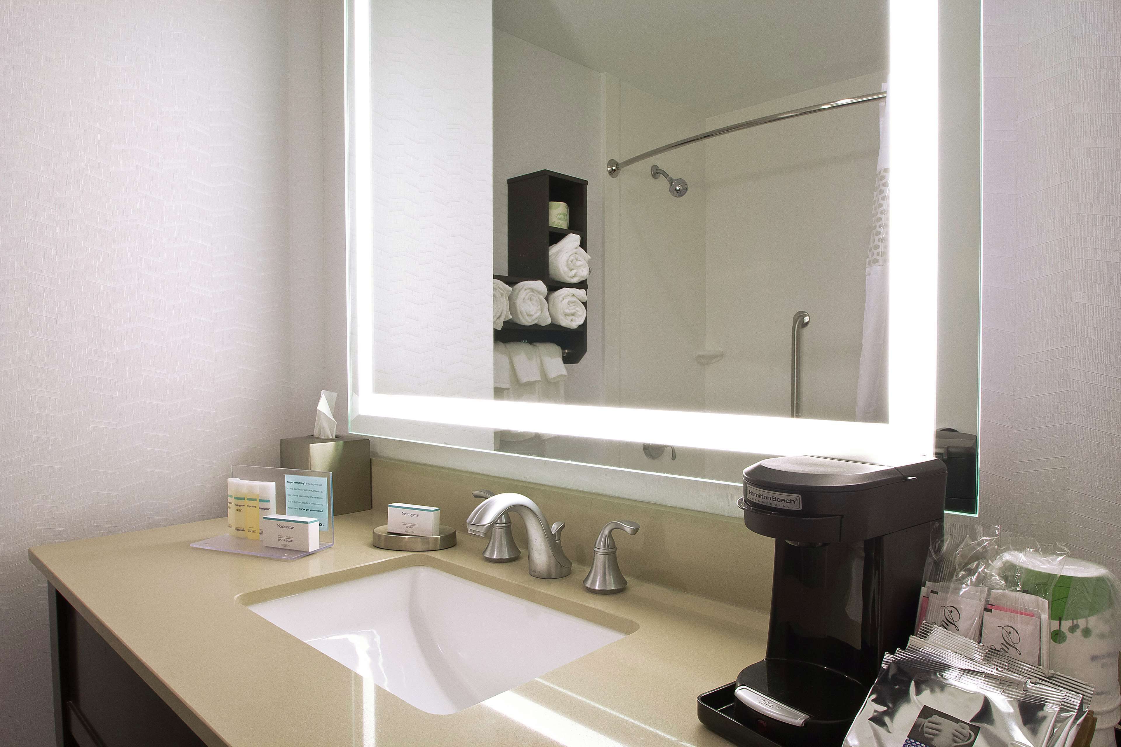 Une salle de bain d’hôtel équipée d’un lavabo, d’un miroir, d’un porte-serviettes et d’une machine à café.
