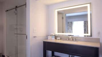 A bathroom with a glass shower enclosure, a vanity with a mirror, and a sink.
