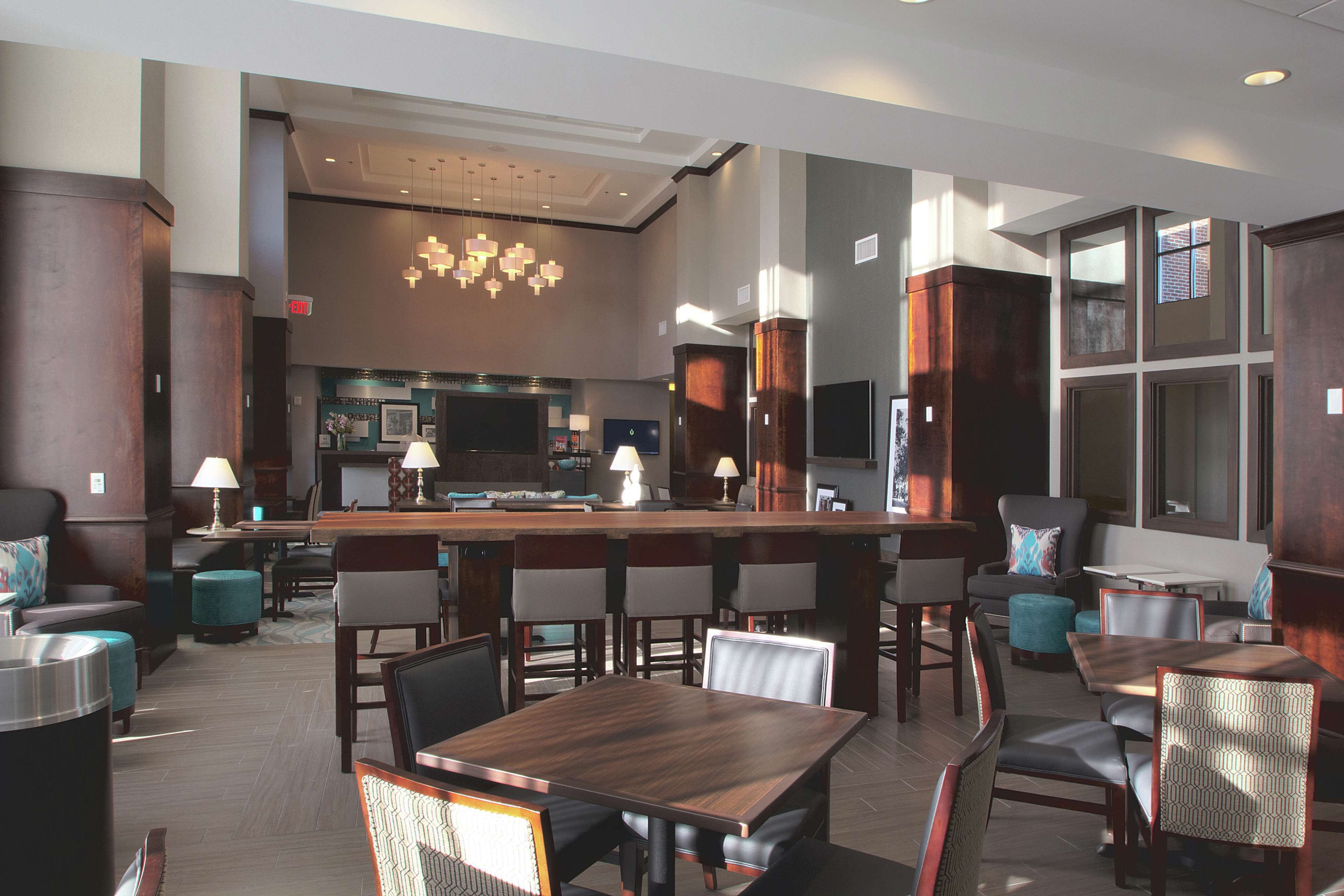 A modern hotel lobby with a bar area, seating arrangements, and a kitchen in the background.