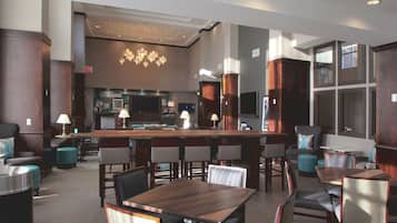 A modern hotel lobby with a bar area, seating arrangements, and a kitchen in the background.