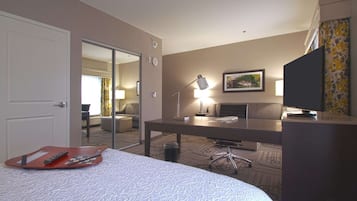 Een hotelkamer met een bed, een bureau, een stoel, een lamp, een televisie en een spiegel.