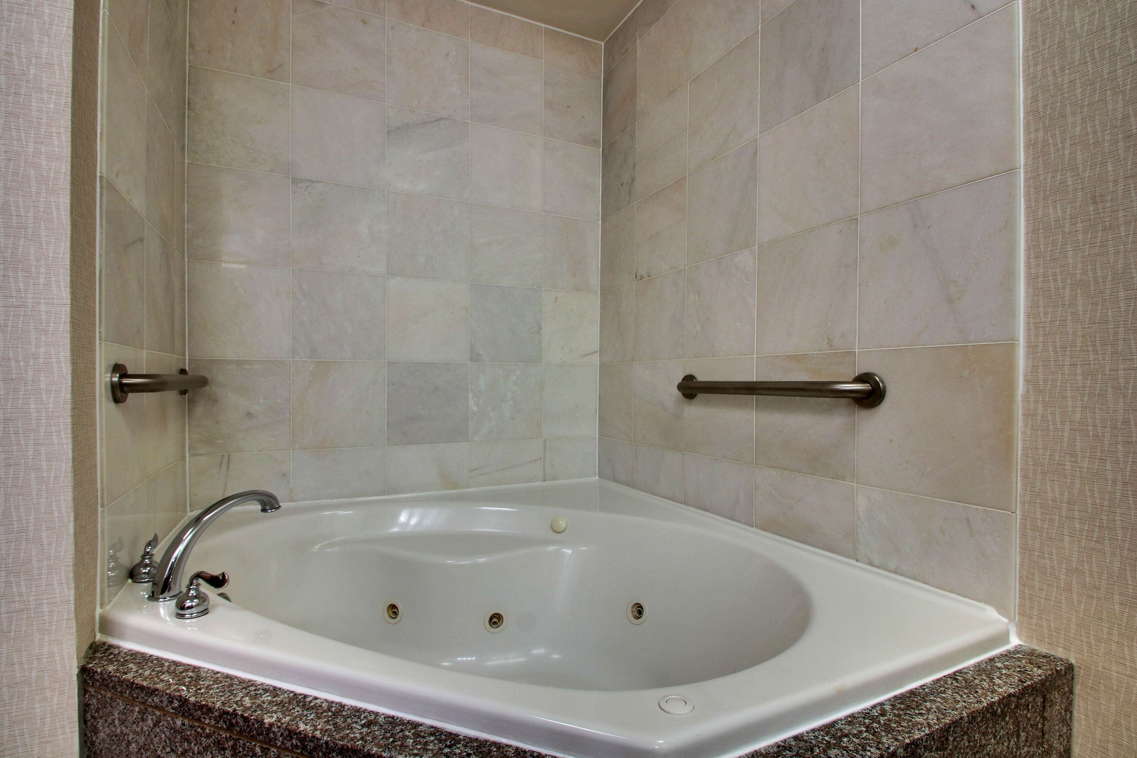A bathroom with a white bathtub, marble tiles, and a granite countertop.