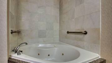 A bathroom with a white bathtub, marble tiles, and a granite countertop.