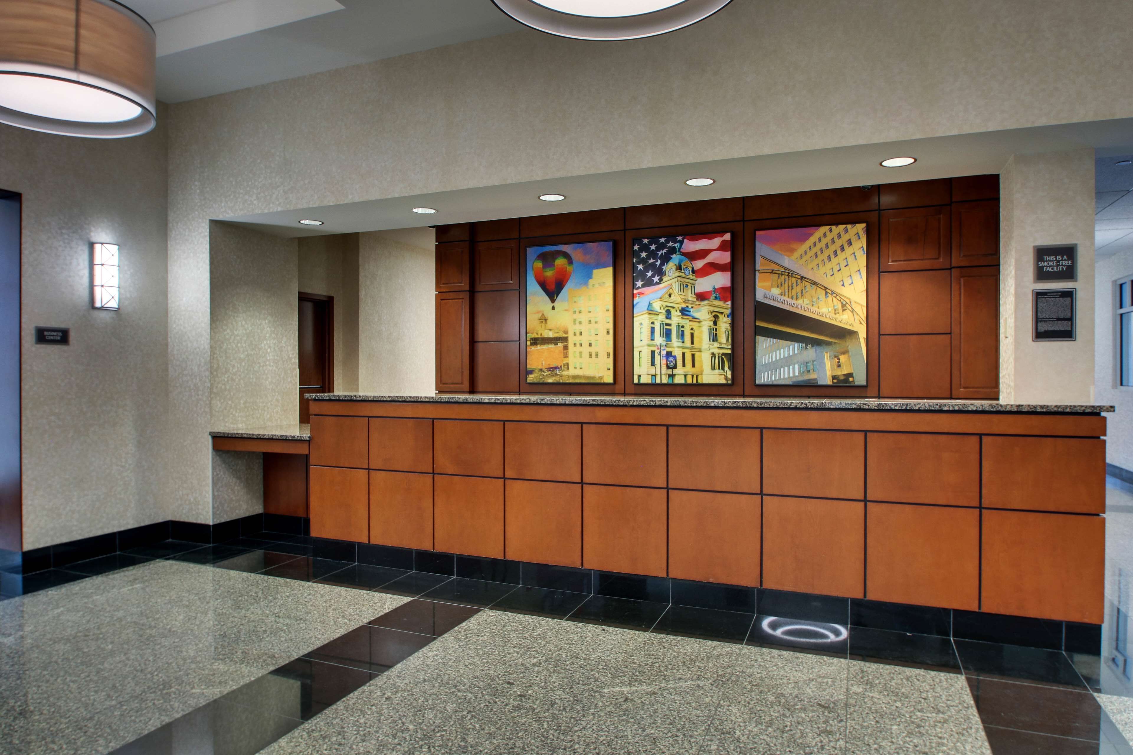 A hotel reception area with a polished granite counter, wooden paneling, and artwork depicting a cityscape and American flag.