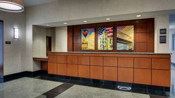 A hotel reception area with a polished granite counter, wooden paneling, and artwork depicting a cityscape and American flag.