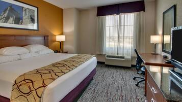 A hotel room with a large bed, a desk, a television, and a window with curtains.