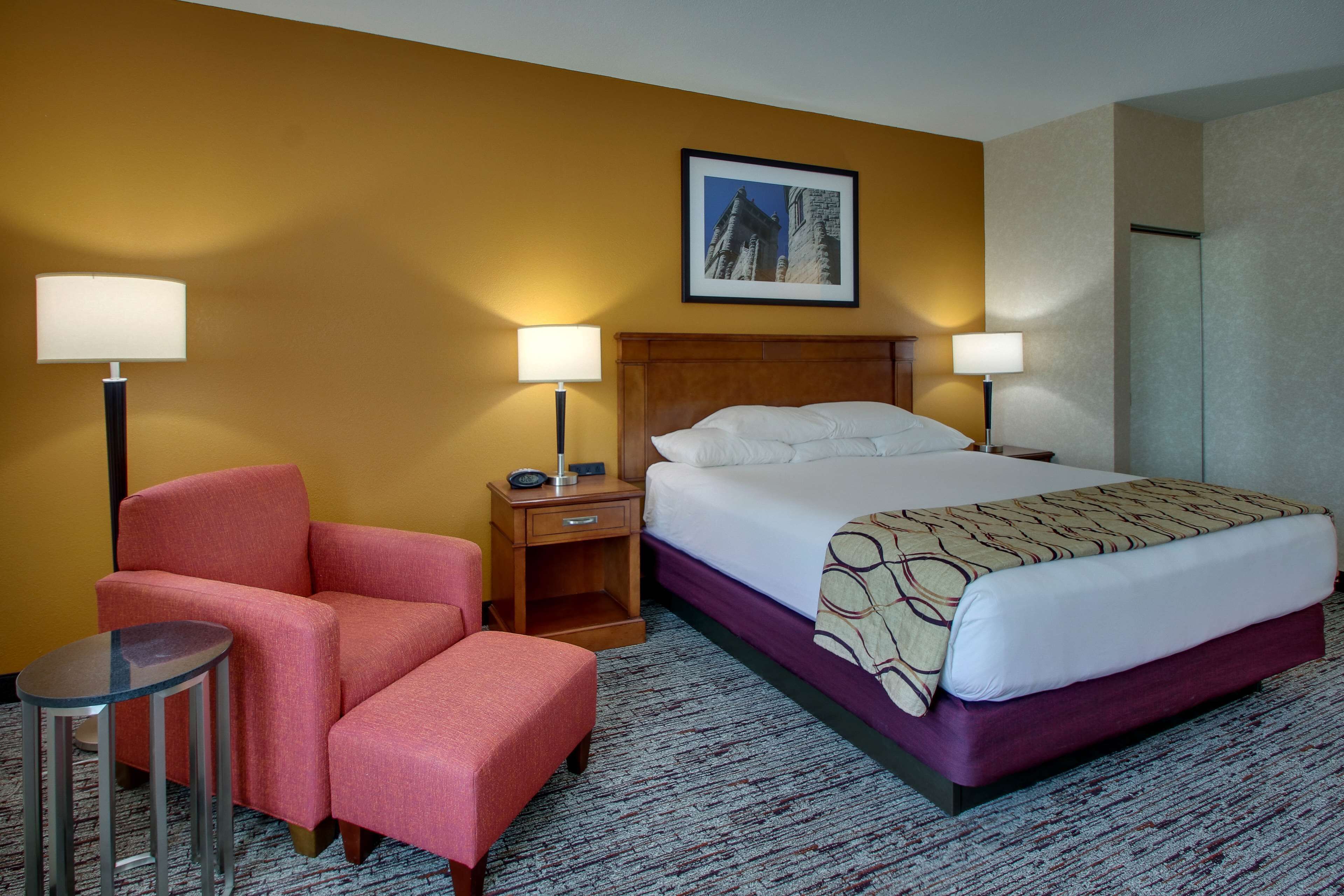 A hotel room with a bed, a chair, a nightstand, and a lamp.