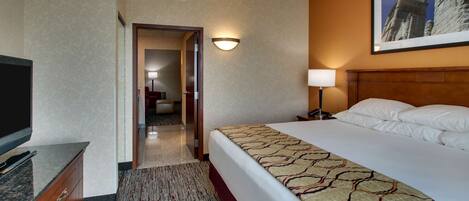 A hotel room with a large bed, a flat-screen TV, a wooden dresser, a carpeted floor, and a framed picture on the wall.