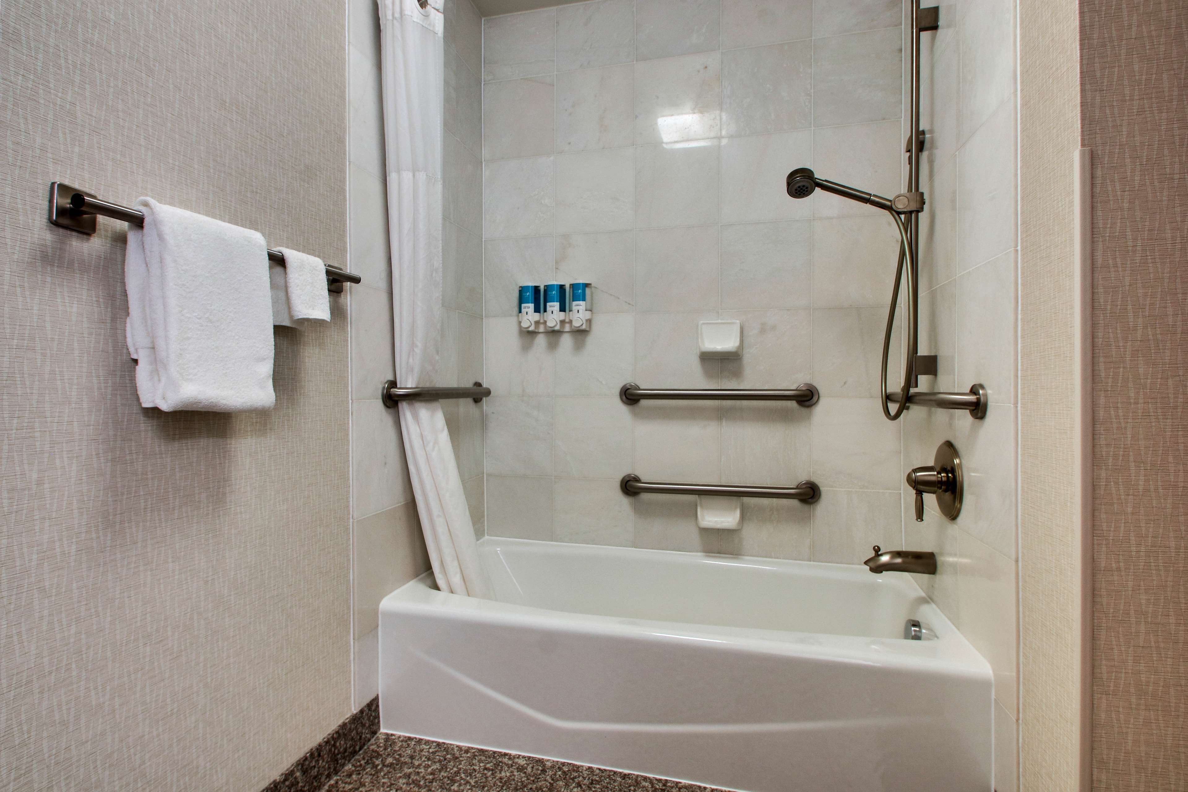 A modern bathroom with a white bathtub, grab bars, a showerhead, and a towel rack.