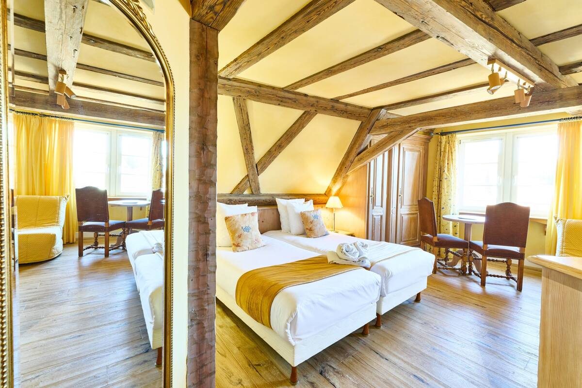 A room with a wooden ceiling, two beds, a table, and chairs.