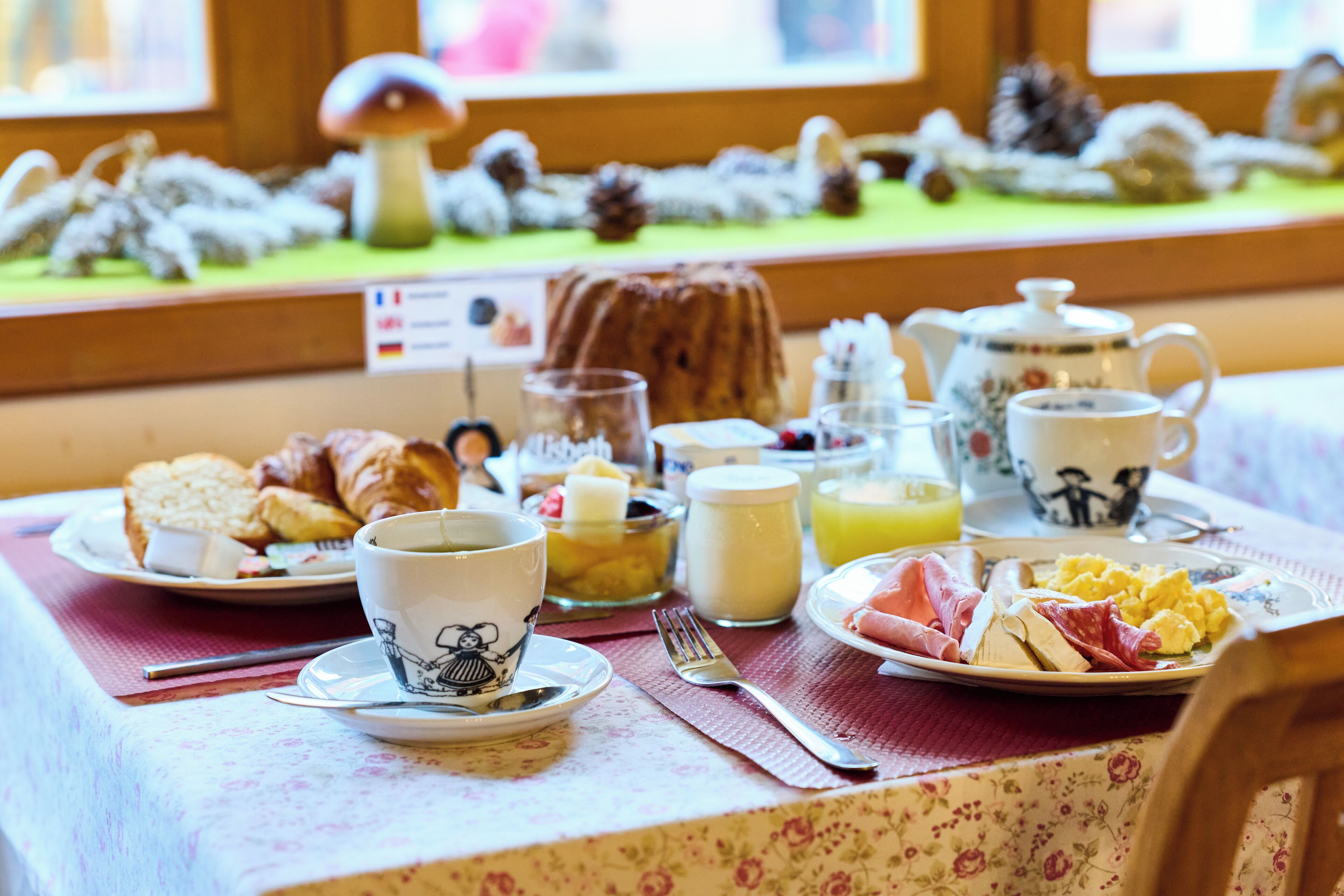 A breakfast table with croissants, eggs, ham, and a tea set.
