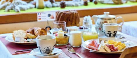 A breakfast table with croissants, eggs, ham, and a tea set.