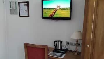A room with a television displaying a giraffe, a small desk with a lamp, and a cabinet.
