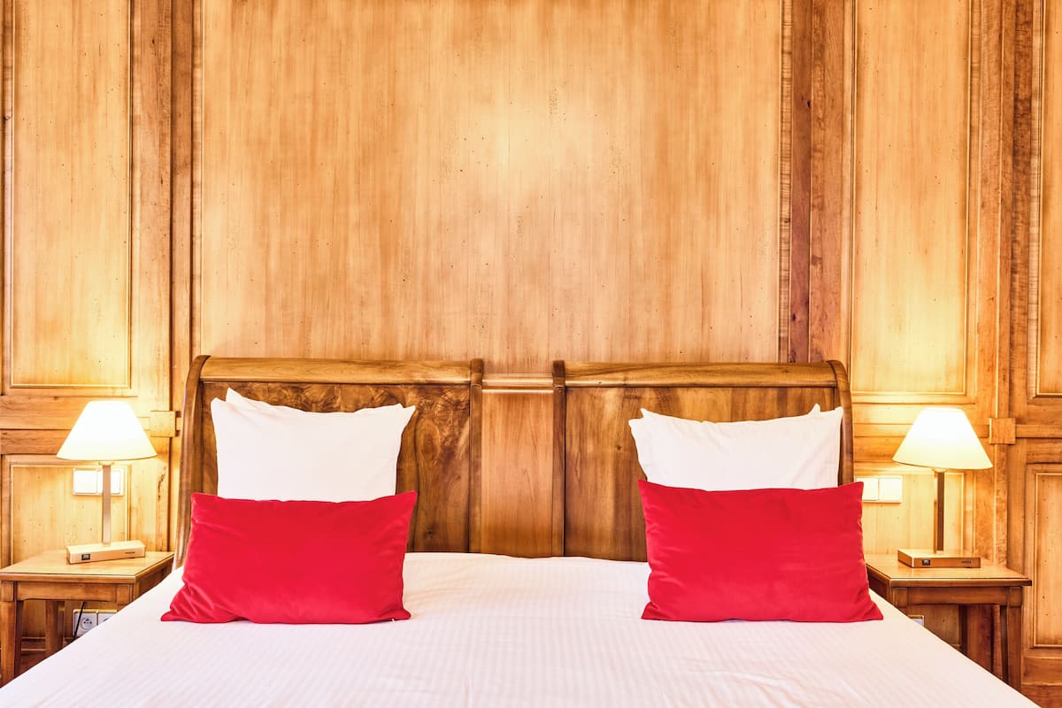 A double bed with white and red pillows, wooden headboard, and two bedside lamps.