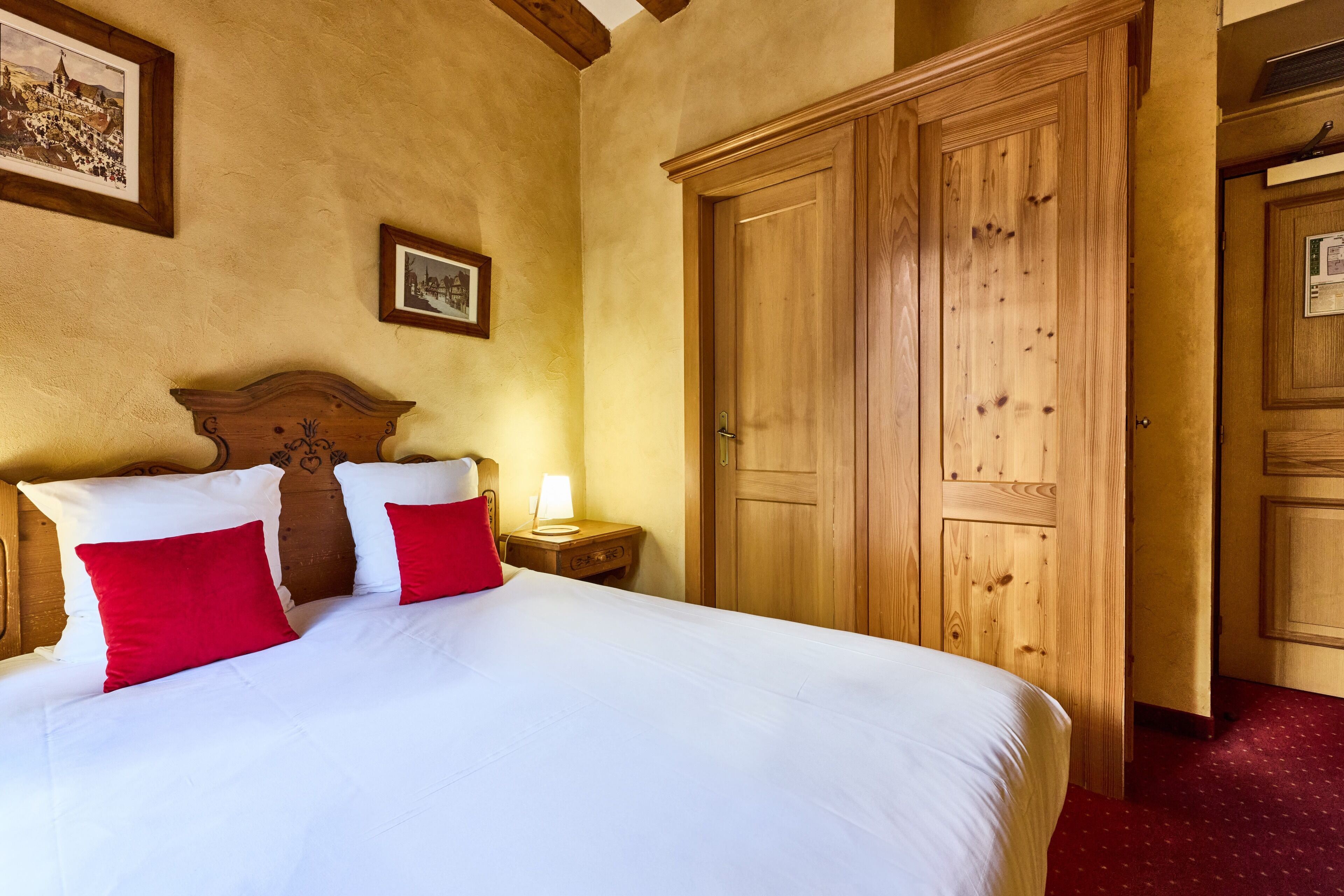 A hotel room with a large bed, wooden wardrobe, and a nightstand with a lamp.