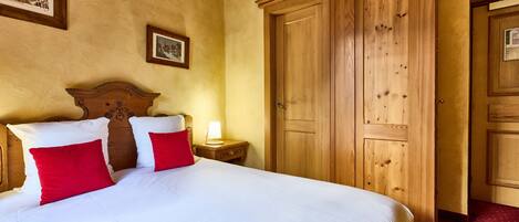 A hotel room with a large bed, wooden wardrobe, and a nightstand with a lamp.