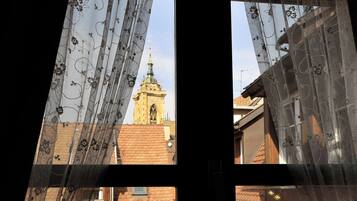 Una finestra con tende in pizzo, vista su un edificio con una torre e un tetto a tegole.