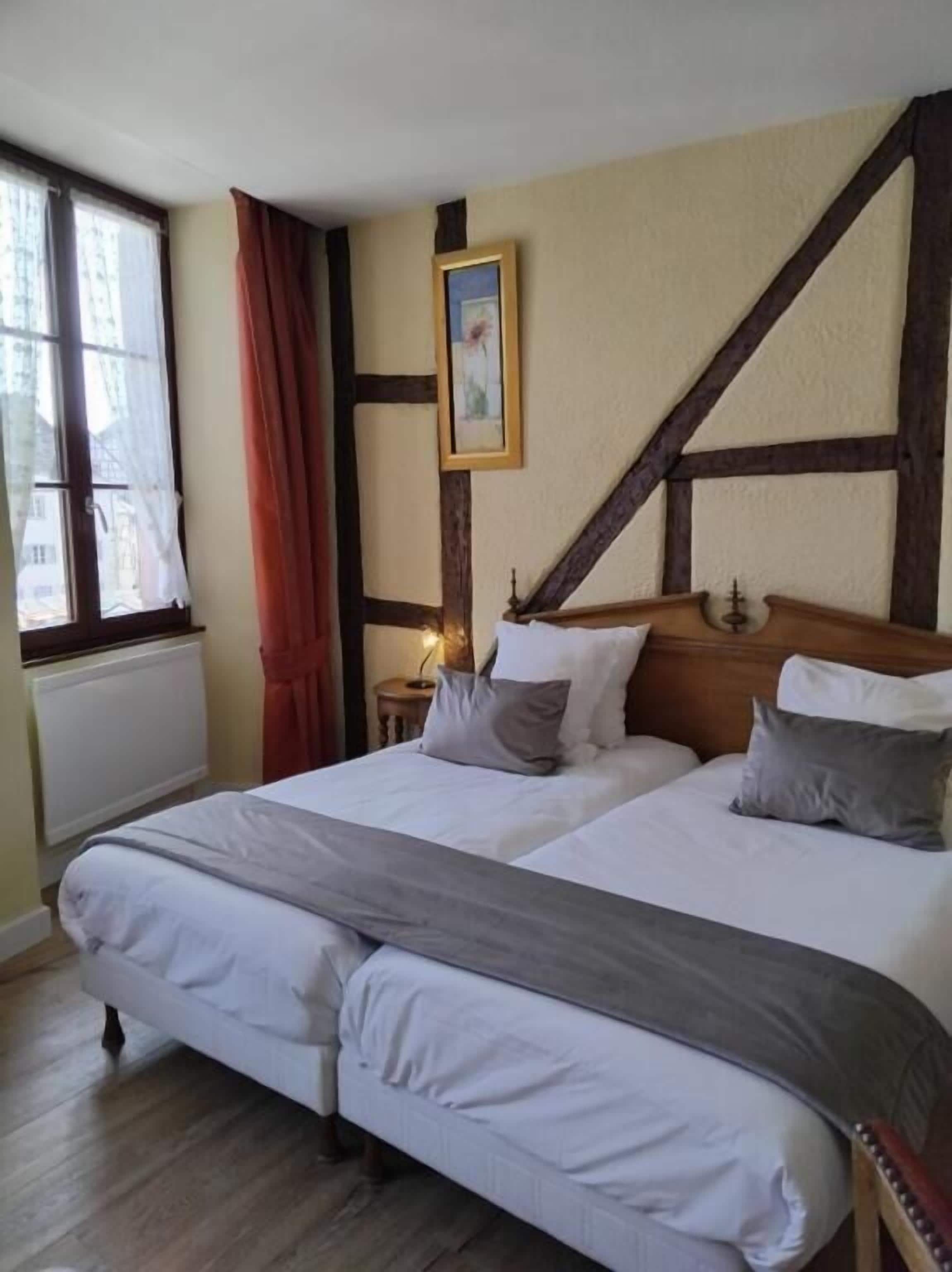 A double bed with a wooden headboard, a nightstand, a framed picture, and a window with curtains.