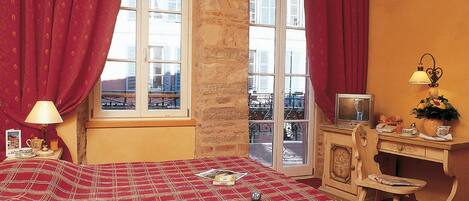 A room with a bed, a desk, a television, and a window with curtains.