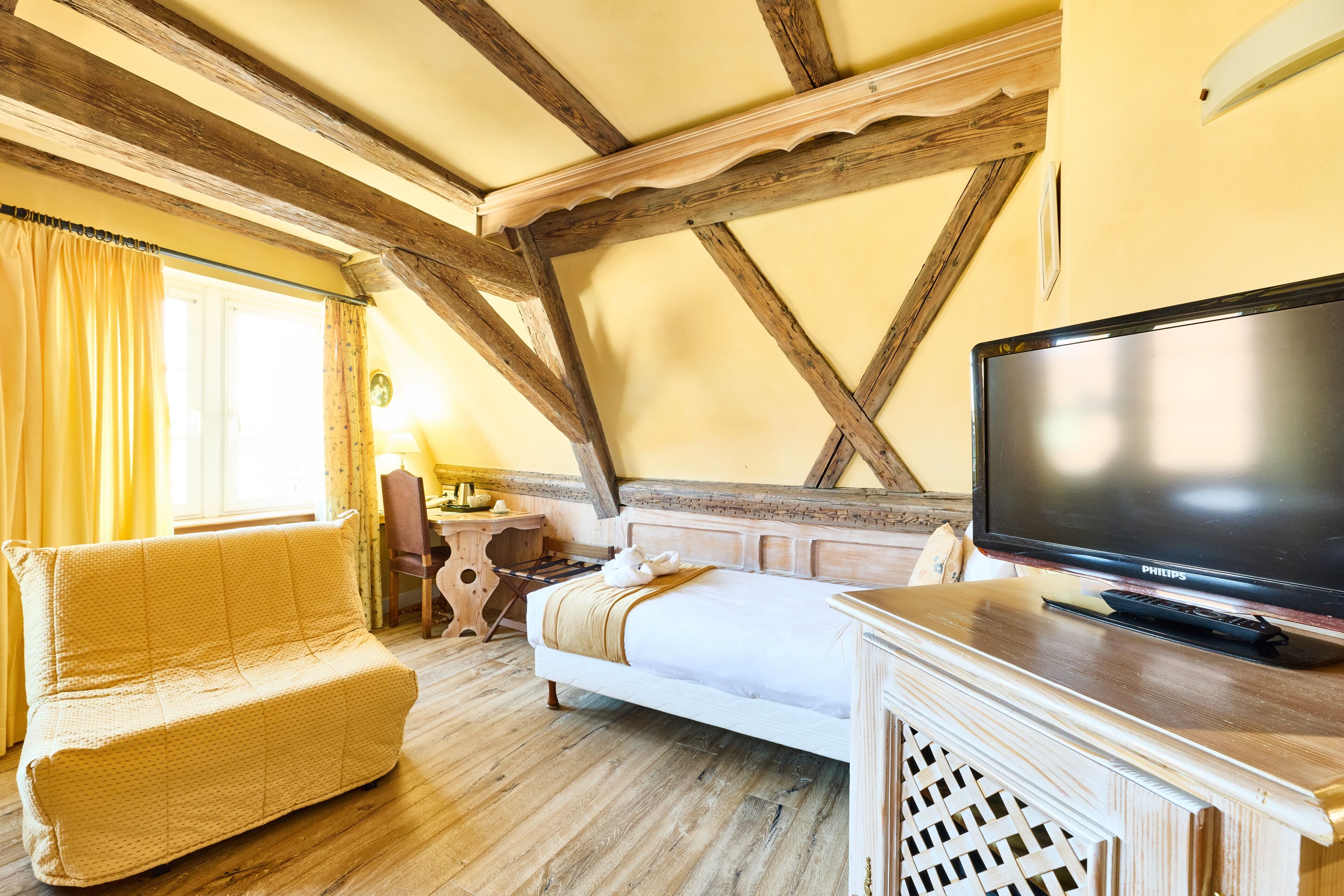 A cozy room with a bed, a wooden bench, a television, and a window with curtains.