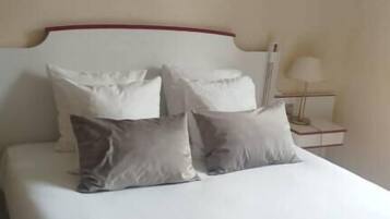 A neatly made bed with white and grey bedding, a red headboard, and a painting of buildings on the wall.