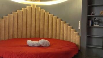 A modern bedroom with a circular headboard, a red bedspread, and a built-in bookshelf.