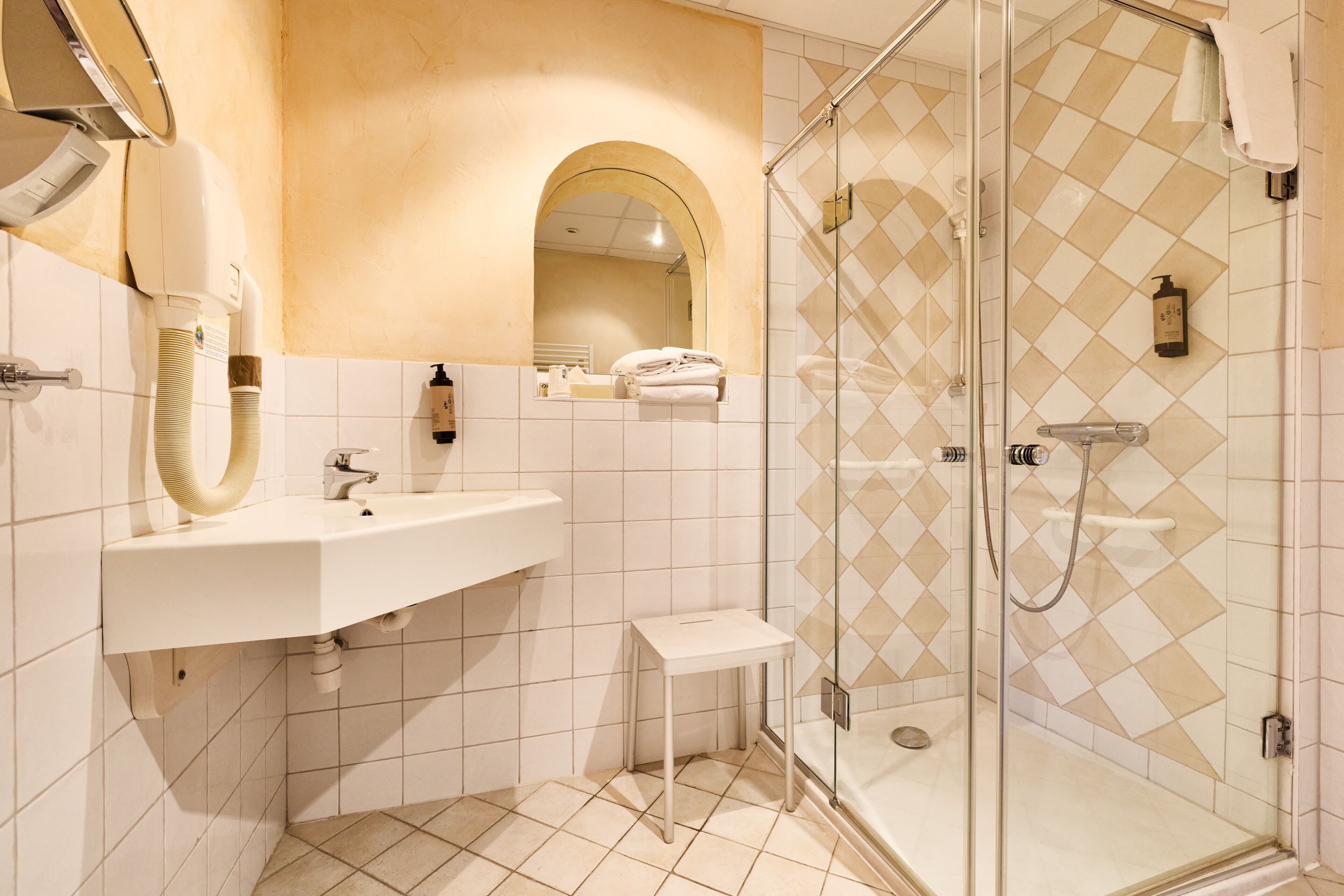 A modern bathroom with a glass-enclosed shower, a white sink, and a small vanity table.