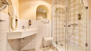 A modern bathroom with a glass-enclosed shower, a white sink, and a small vanity table.