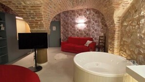 Una habitación con techo de piedra, un sofá rojo, una bañera blanca y un televisor.