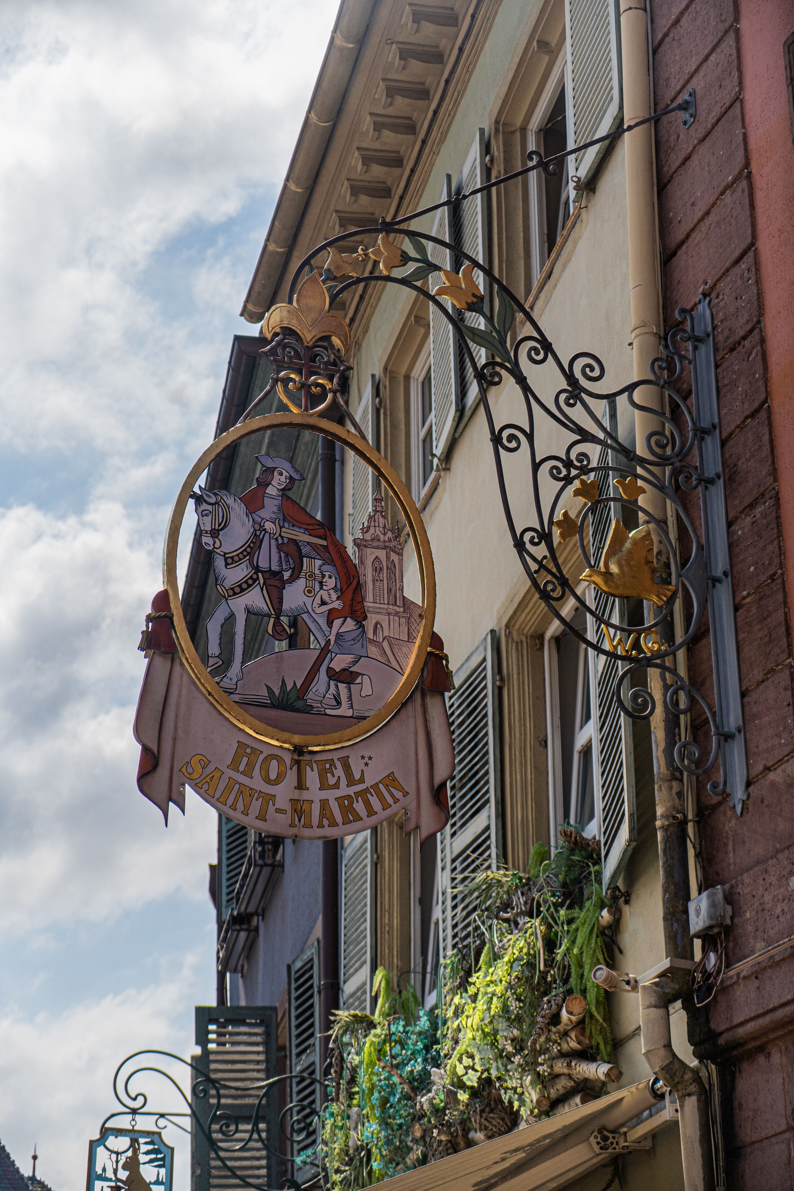 A hotel sign with a knight and horse emblem, a banner with the hotel's name, and a decorative metalwork design.