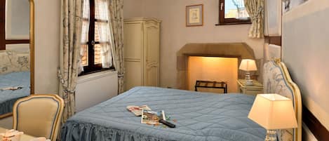 A bedroom with a large bed, a bedside table with a lamp, a telephone, a chair, a wardrobe, and a mirror.
