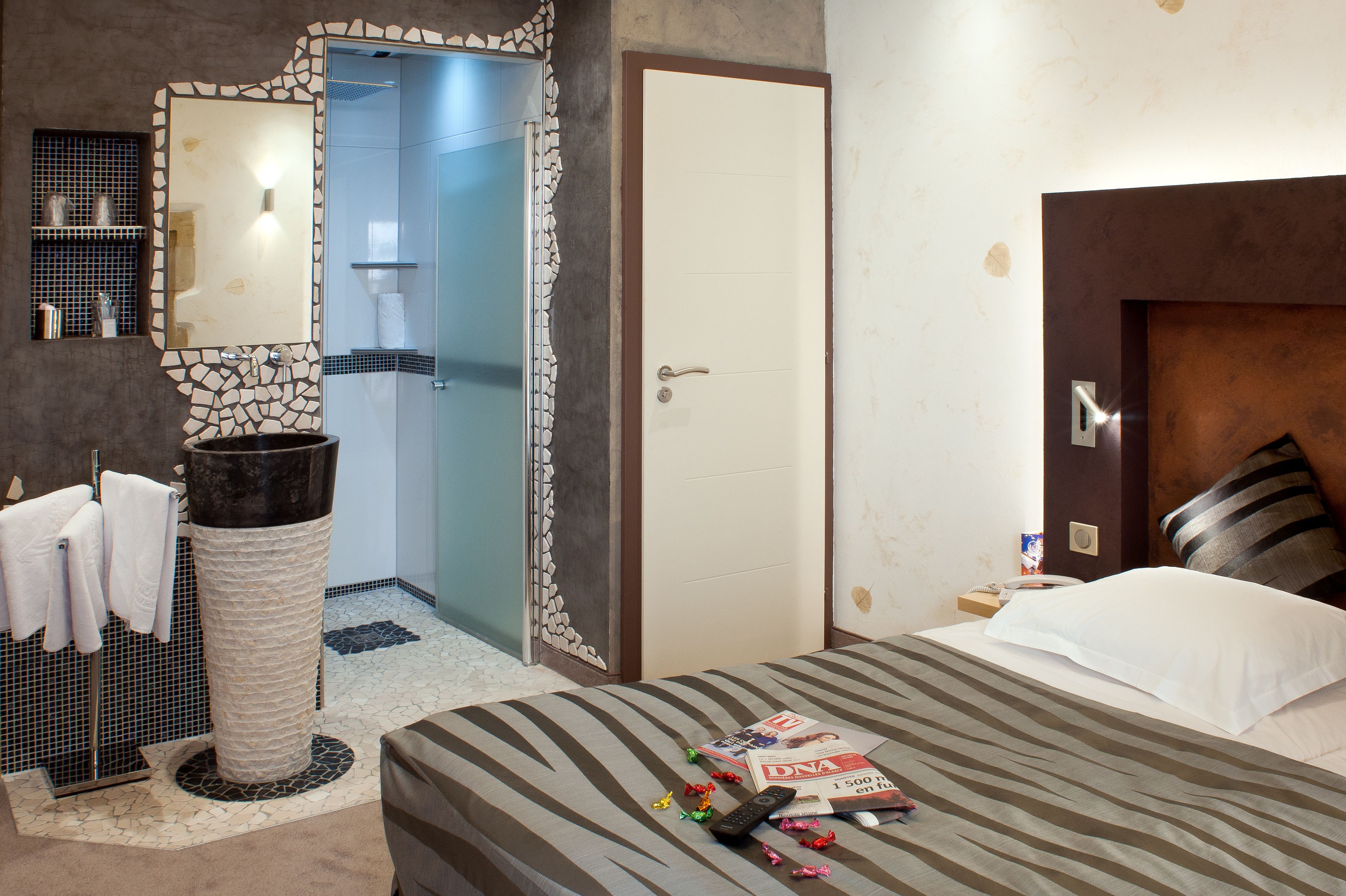 A hotel room with a bed, a bathroom with a shower, a sink, and a mirror.