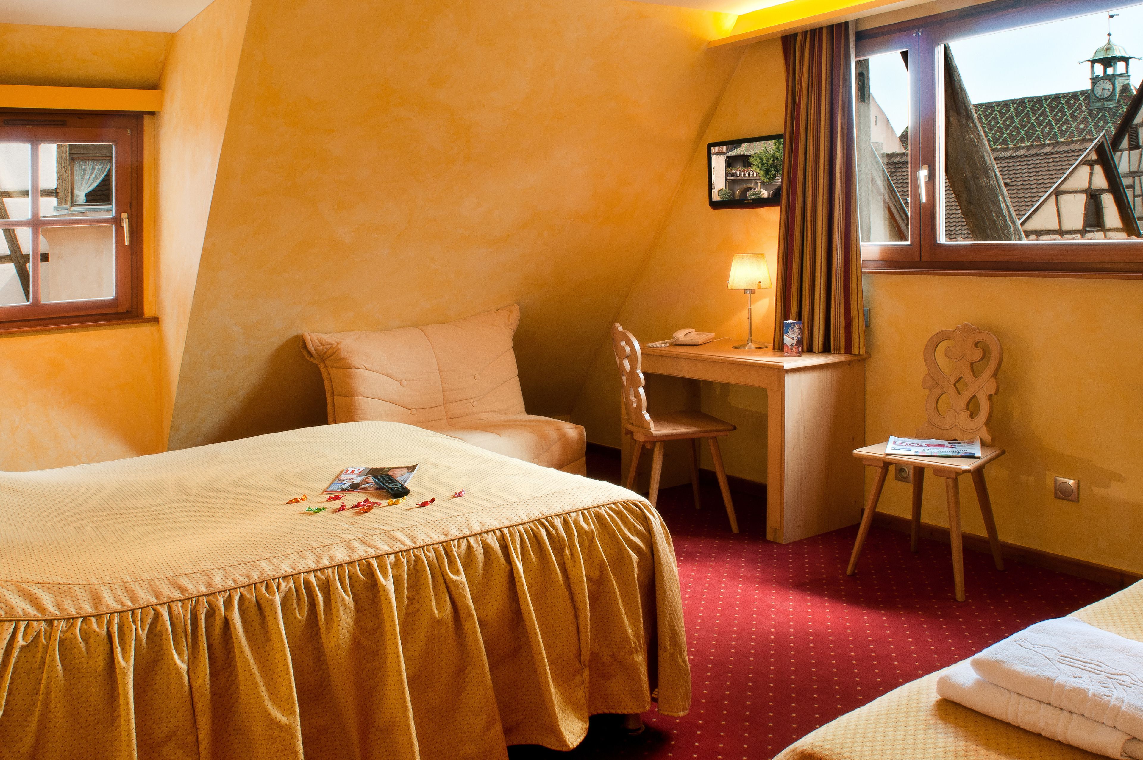 A hotel room with a bed, a desk, a chair, and a window with a view of buildings.