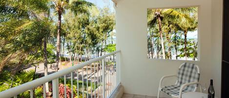 A balcony with a white railing, a checkered chair, a small round table, and a bottle of wine.