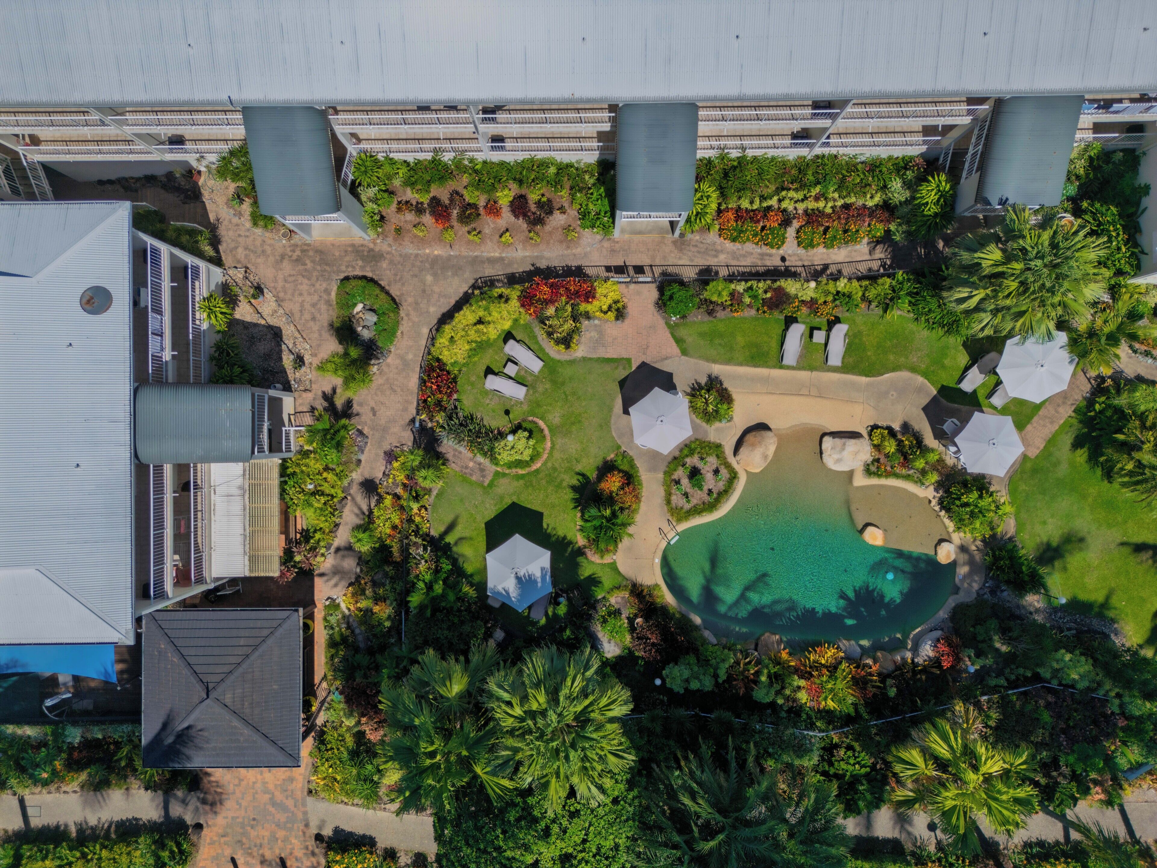An aerial view of a resort with a swimming pool, lounge areas, and lush landscaping.
