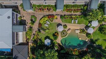 An aerial view of a resort with a swimming pool, lounge areas, and lush landscaping.