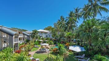 A resort with a pool area, lounge chairs, and a garden with palm trees.