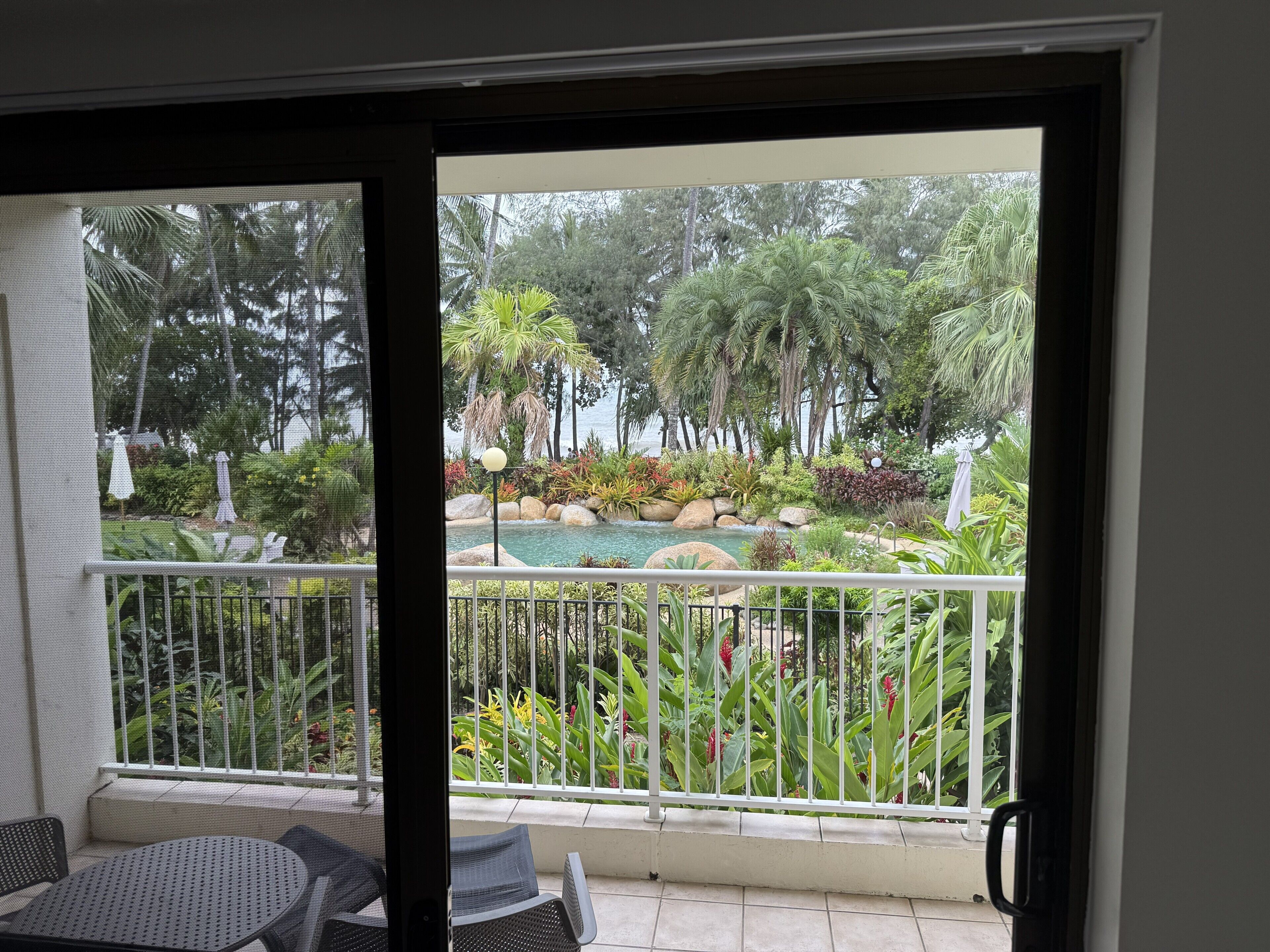 Ein Balkon mit Blick auf einen angelegten Garten, inklusive Pool und unterschiedlicher Pflanzen.